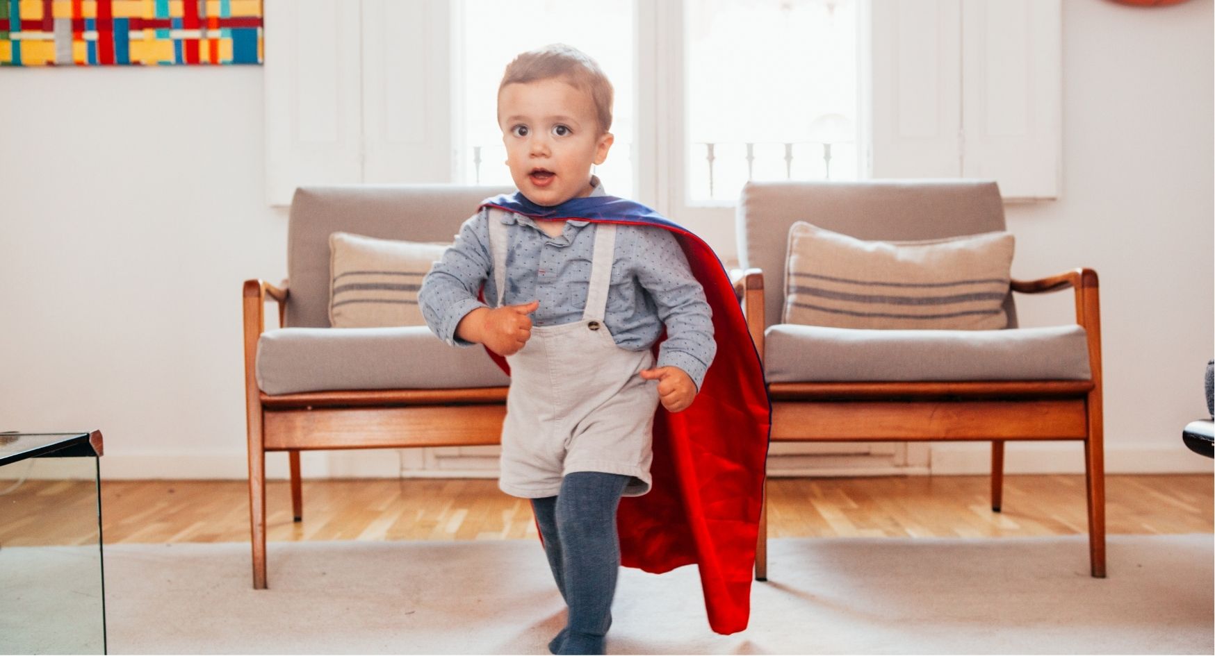 Little boy with cape running with chairs in background